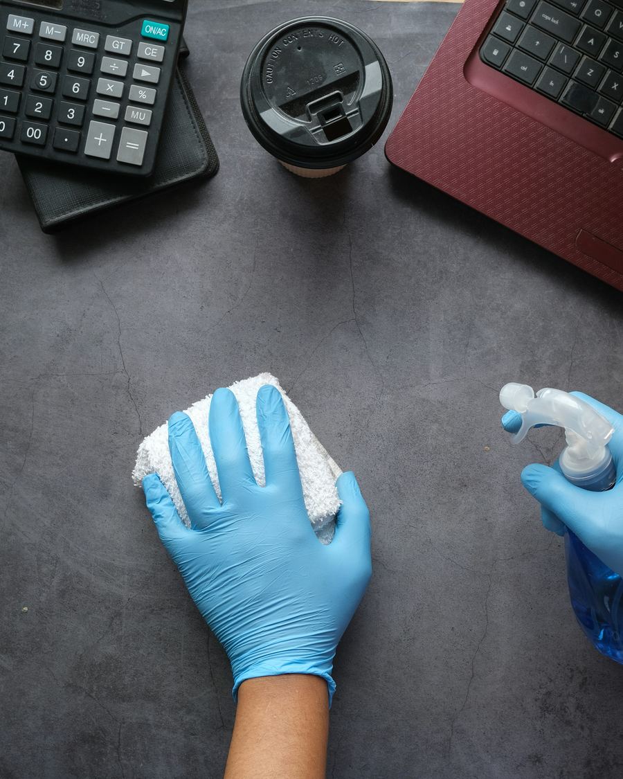 Reinigungskraft desinfiziert eine Schreibtischoberfläche mit Handschuhen und Mikrofasertuch